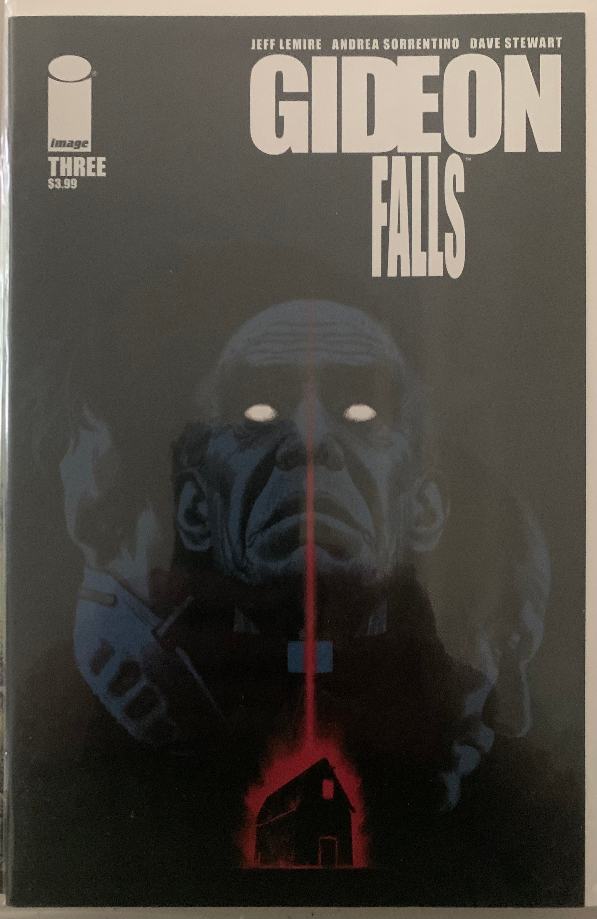 Comic book cover of 'Gideon Falls' with a dark background and a figure of a priest with glowing eyes over a ominous glowing red barn.