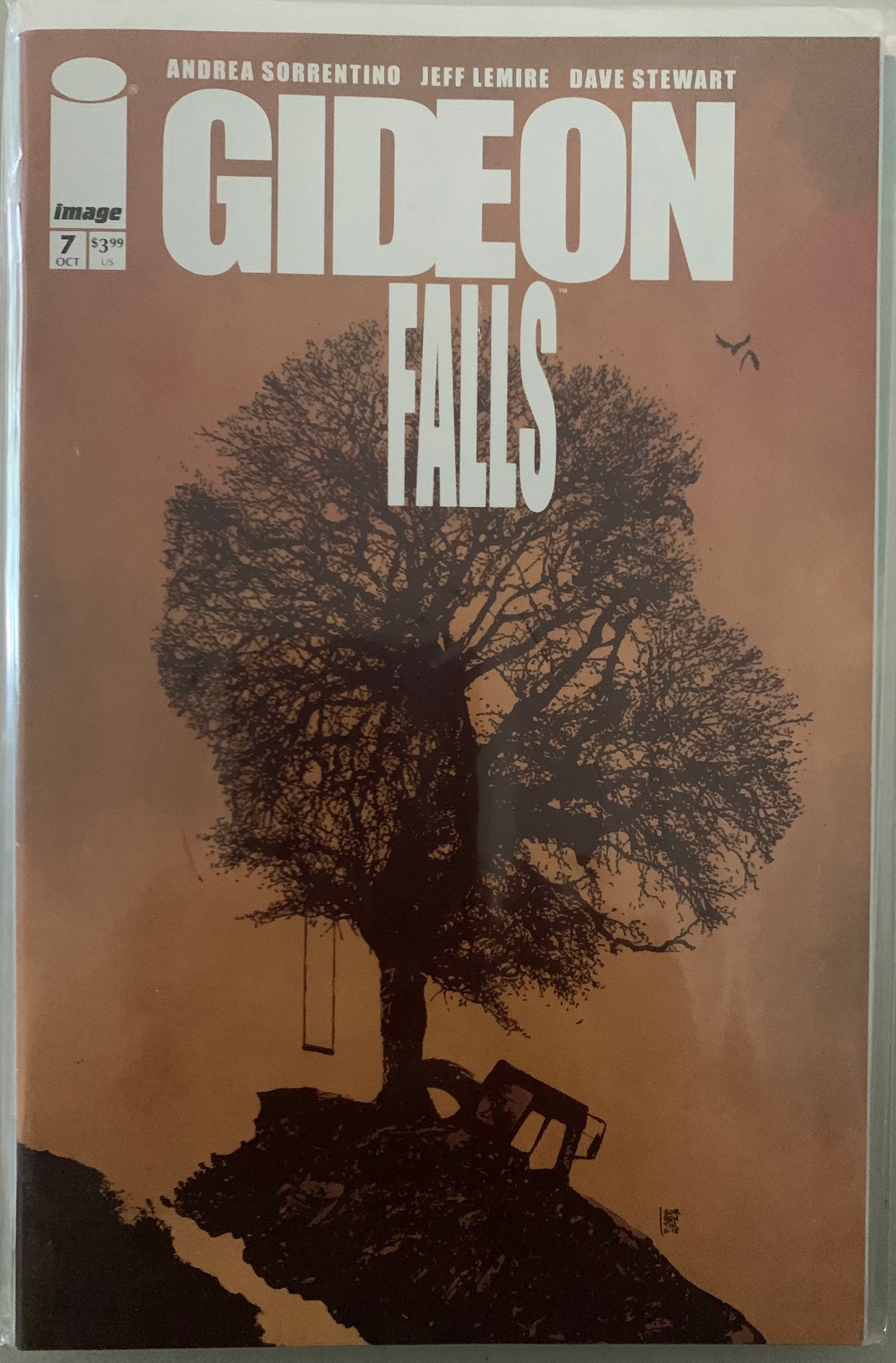 Comic book cover of 'Gideon Falls' with a tree in the shape of a masked man's head and swing on a brown background