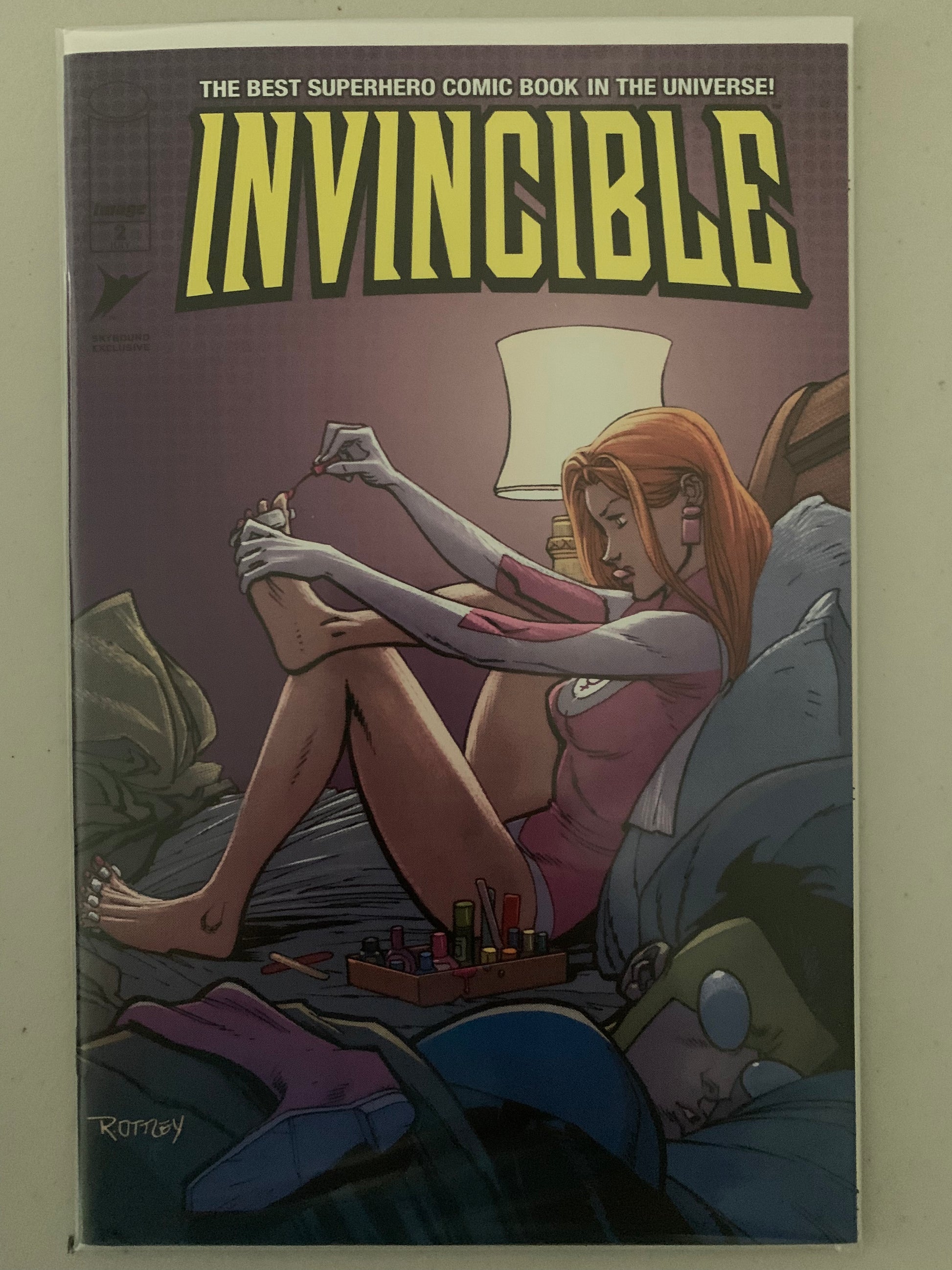 Comic book cover of 'Invincible' sleeping with Atom Eve applying toenail polish in bed beside him.